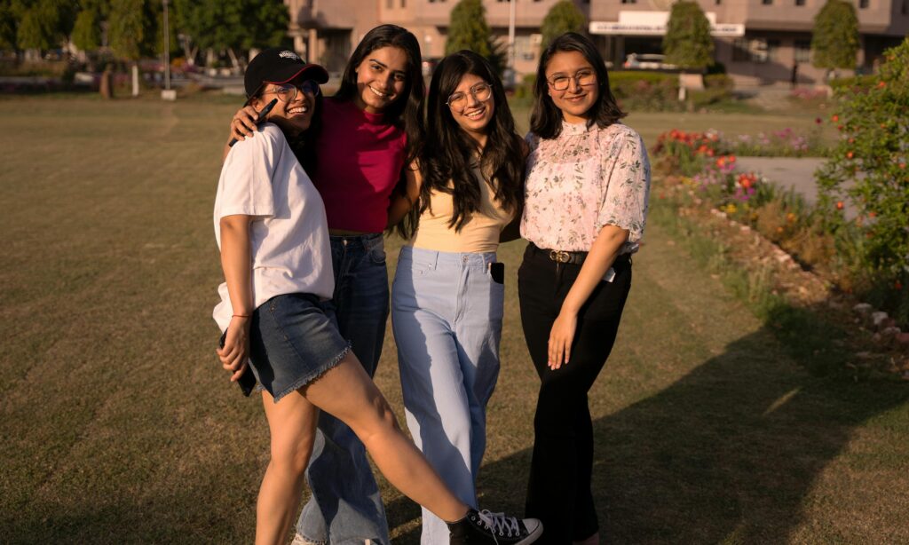 Smiling friends posing together in a park during a warm sunny day, showcasing vibrant styles and camaraderie.